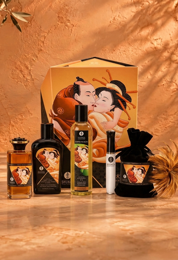 Shunga gift set with bottles, pouch, feather and illustrated gift bag against a warm terracotta wall