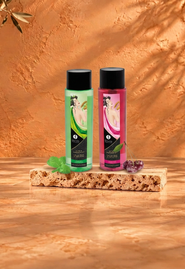 Green and pink Shunga bath and shower bottles on travertine with botanical shadows and burgundy fabric