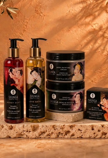 Shunga massage oil bottles, cream jars and boxed massage candle on travertine against a warm terracotta wall