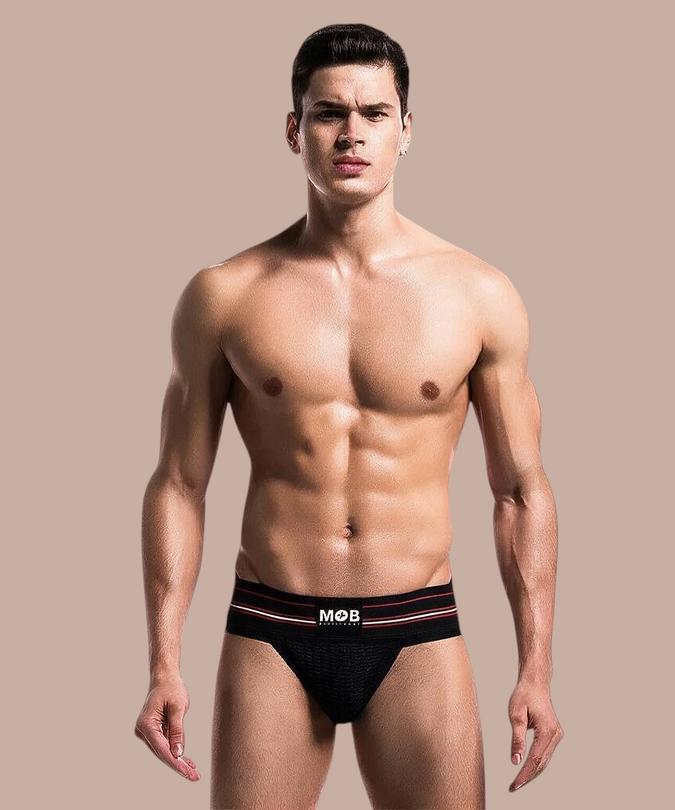 Model draagt een zwarte MOB Classic thong met een elastische tailleband van Pleasurements in een studio-opstelling.
