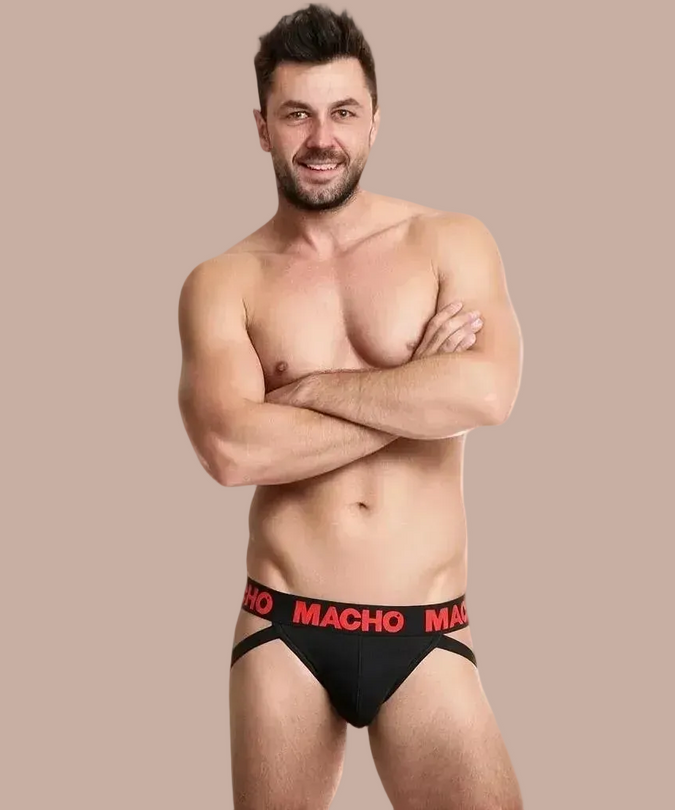 Pleasurements Macho MX26X2 jockstrap in zwart met rode tailleband gedragen door een model met gekruiste armen.