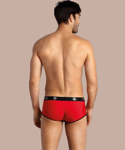 Anais Men – Soul Slip S Pleasurements Anais Men Soul Brief in rood met zwarte tailleband en logo, gedragen door een glimlachend model.