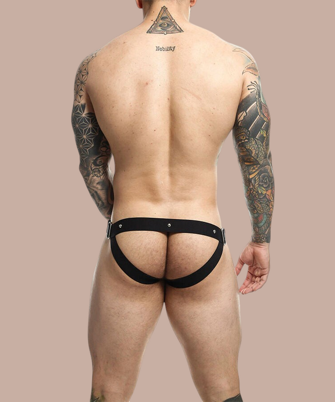 Pleasurements Mob Dngeon jockstrap in zwart leer met metalen accenten gedragen door een getatoeëerde man van achteren