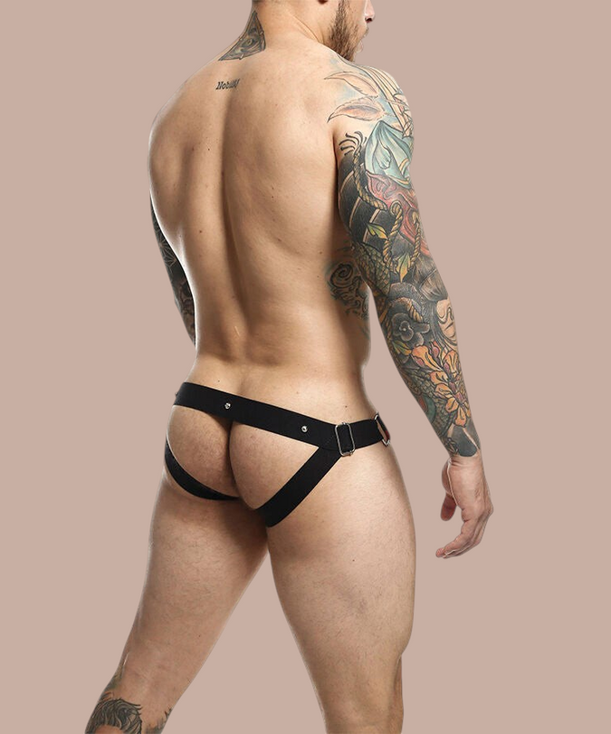 Pleasurements Mob Dngeon jockstrap met cockring in zwart leer en metaal, gedragen door een getatoeëerde man.