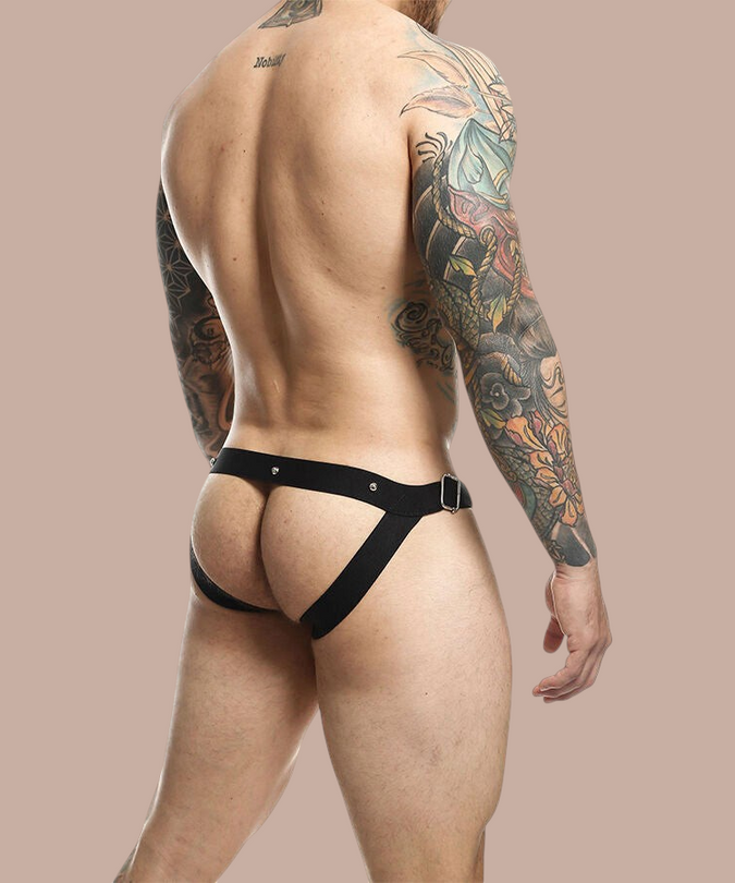 Pleasurements Mob Dngeon Snap jockstrap in zwart leer met metalen details gedragen door een getatoeëerde man