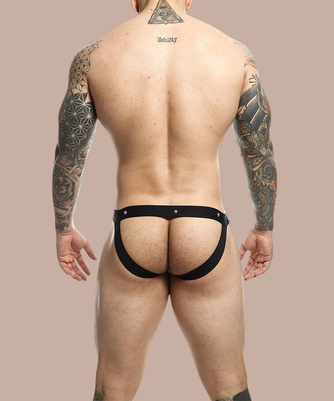 Pleasurements Mob Dngeon Snap jockstrap in zwart leer met metalen drukknopen gedragen door een getatoeëerde man