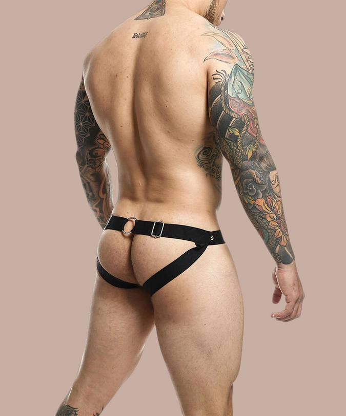 Pleasurements Mob Dngeon jockstrap in zwart leer met metalen ringen gedragen door een getatoeëerde man van achteren