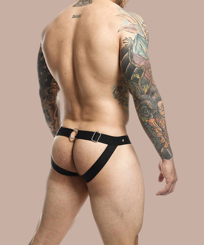 Pleasurements Mob Dngeon jockstrap in zwart leer met metalen ringen gedragen door een getatoeëerde man