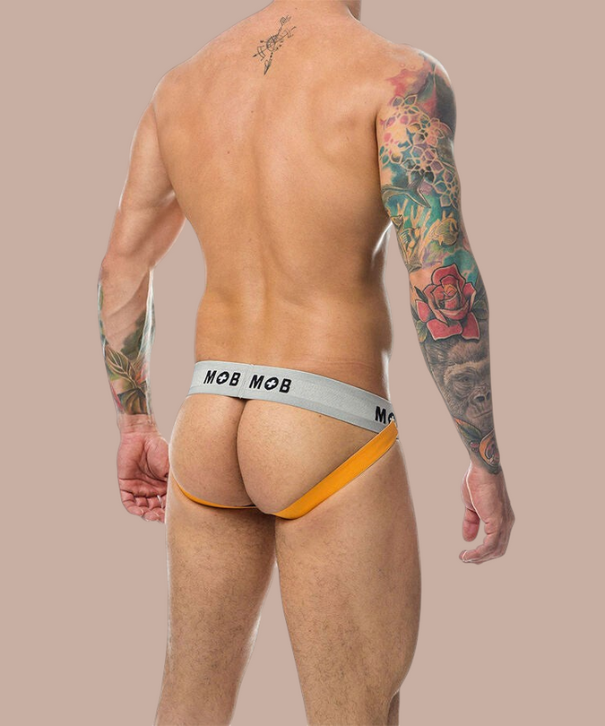 Pleasurements Mob Classic Jockstrap in oranje met grijze tailleband gedragen door een man met tatoeages