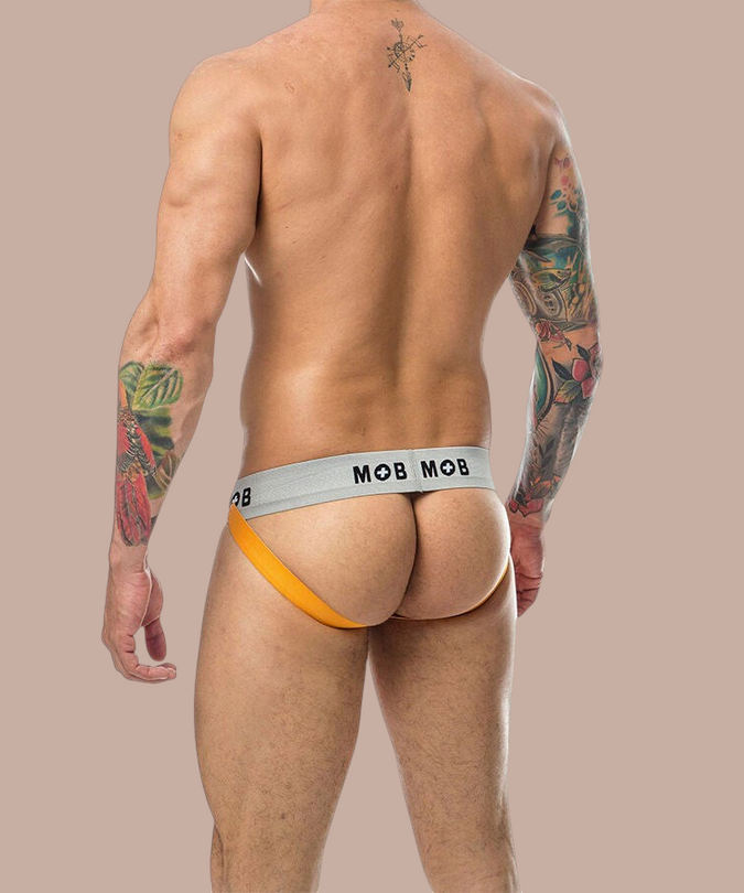 Pleasurements Mob Classic Jock Stripe in oranje met grijze tailleband gedragen door een getatoeëerde man van achteren
