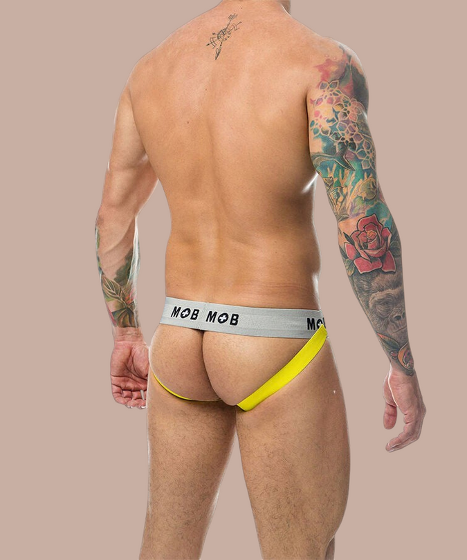Pleasurements Mob Classic Jock Stripe in geel met grijze tailleband gedragen door een man met tatoeages op de rug