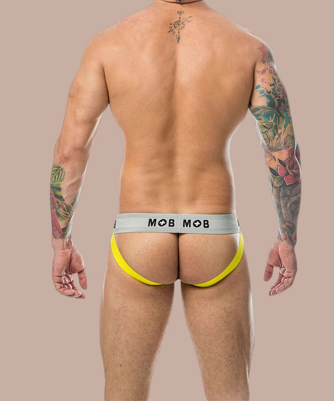 Achterkant van een gele Mob Classic Jock Stripe met grijze tailleband gedragen door een getatoeëerde man.