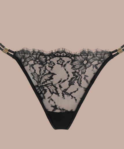 Atelier Amour – Sans Détour Thong Black Pleasurements Atelier Amour Sans Détour zwarte string met verfijnd kant en dunne tailleband gedragen door een model