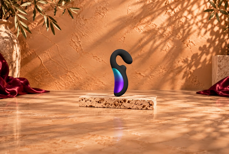 Black vibrator with a colourful accent on a light travertine slab, against a warm copper-beige background with burgundy satin