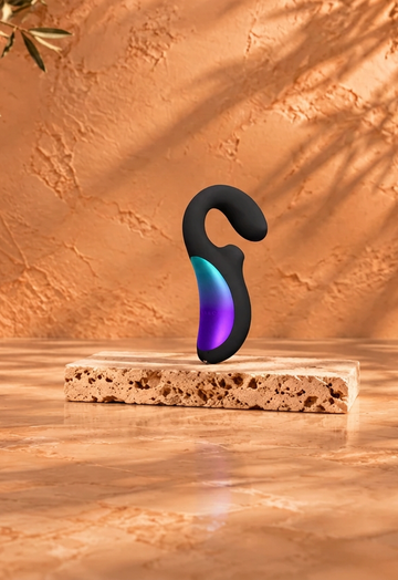 Black vibrator with a colourful accent on a light travertine slab, against a warm copper-beige background with burgundy satin