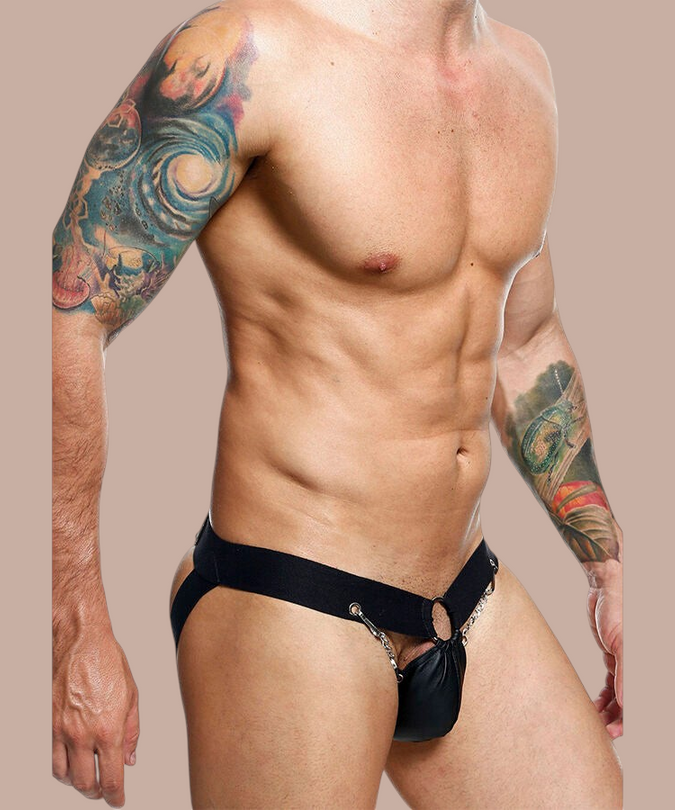 Pleasurements Mob Dngeon zwarte leren jockstrap met metalen kettingdetails gedragen door een getatoeëerde man