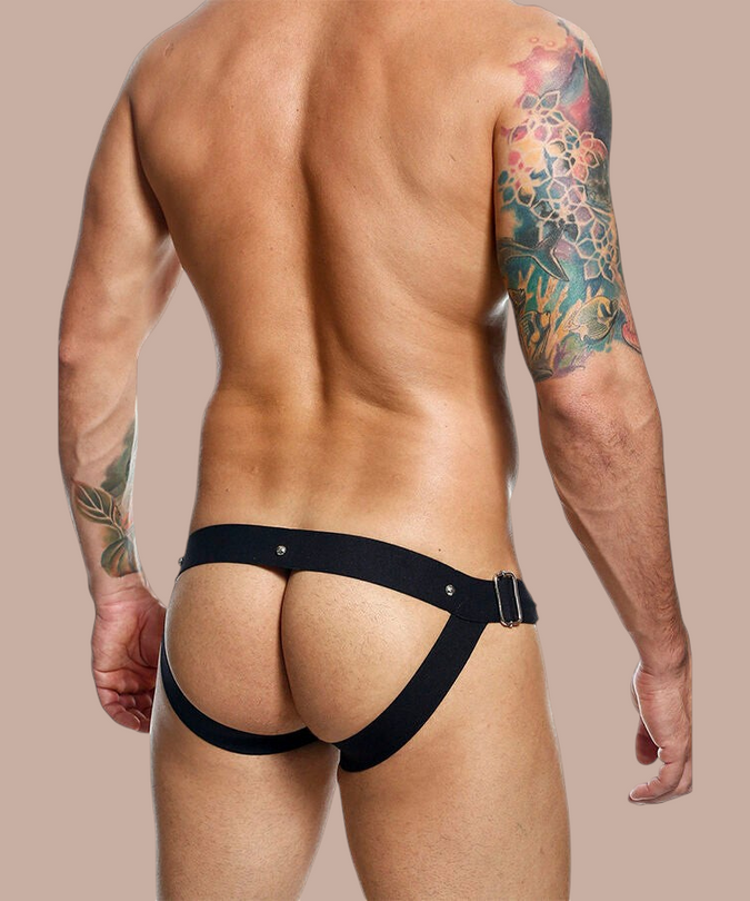 Pleasurements Mob Dngeon jockstrap in zwart leer en metaal, gedragen door een man met tatoeages op de rug en armen.