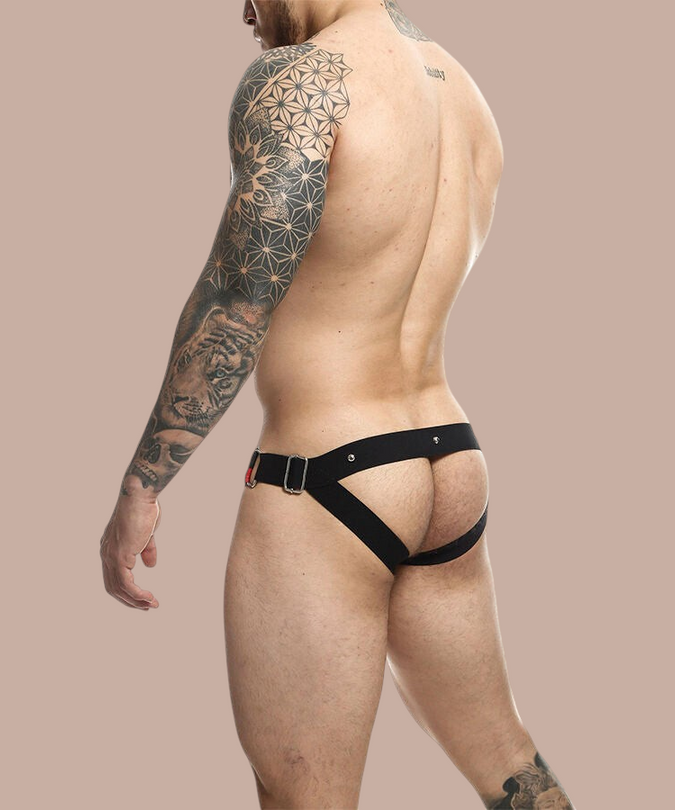 Pleasurements Mob Dngeon jockstrap met rode accenten en metalen ringen gedragen door een getatoeëerde man