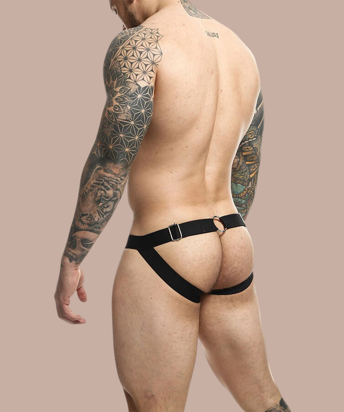 Pleasurements Mob Dngeon zwarte jockstrap met metalen ringen en kettingdetails gedragen door een getatoeëerde man