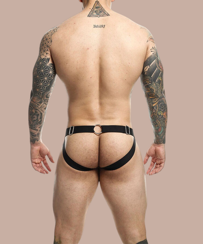 Pleasurements Mob Dngeon jockstrap in zwart met metalen kettingdetails gedragen door een getatoeëerde man