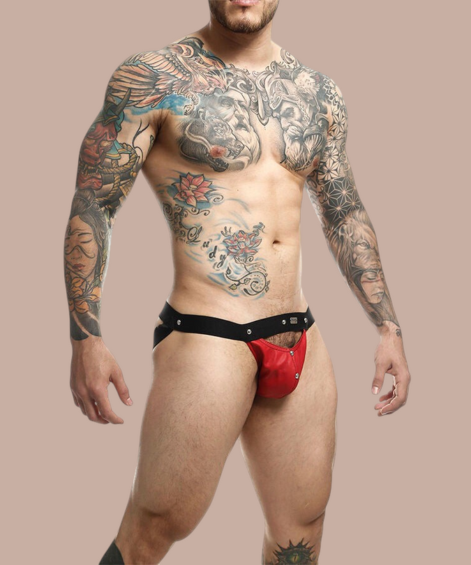 Pleasurements Mob Dngeon jockstrap in rood leer en metaal gedragen door een getatoeëerde man voor een witte achtergrond