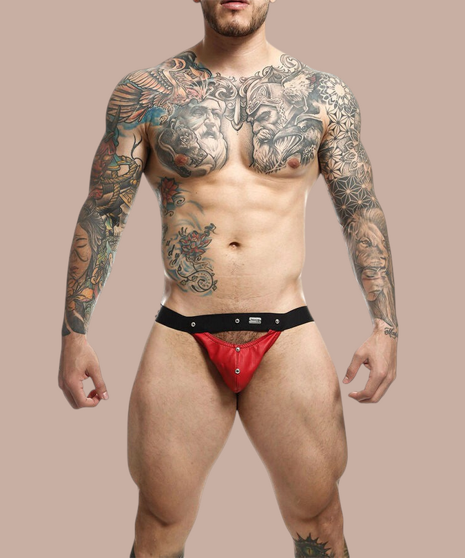 Pleasurements Mob Dngeon jockstrap in rood leer met metalen details gedragen door een getatoeëerde man