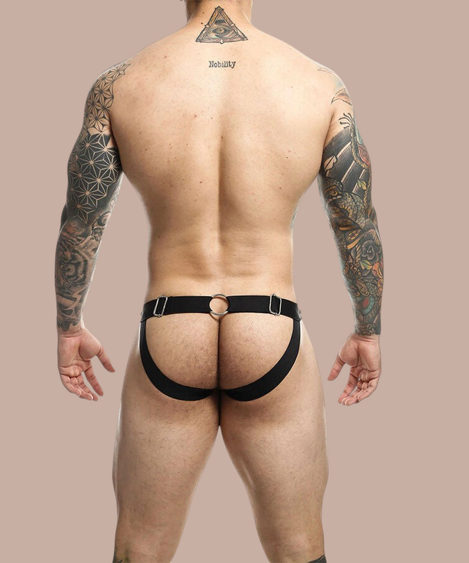 Pleasurements Mob Dngeon jockstrap in zwart leer en metaal, gedragen door een getatoeëerde man van achteren gezien.