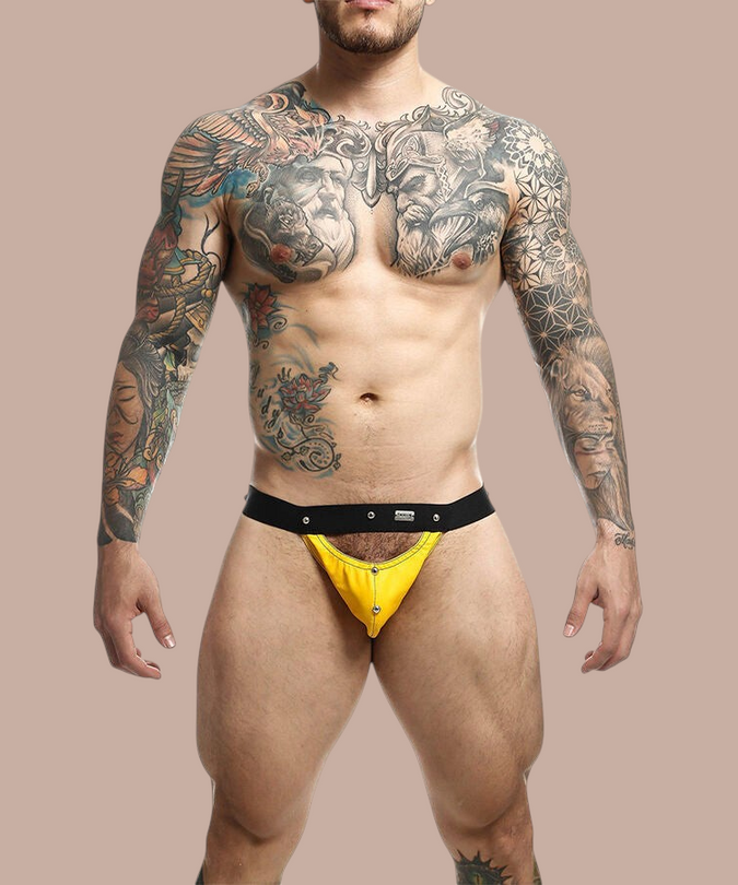 Pleasurements Mob Dngeon jockstrap in geel leer en metaal gedragen door een getatoeëerde man voor een witte achtergrond