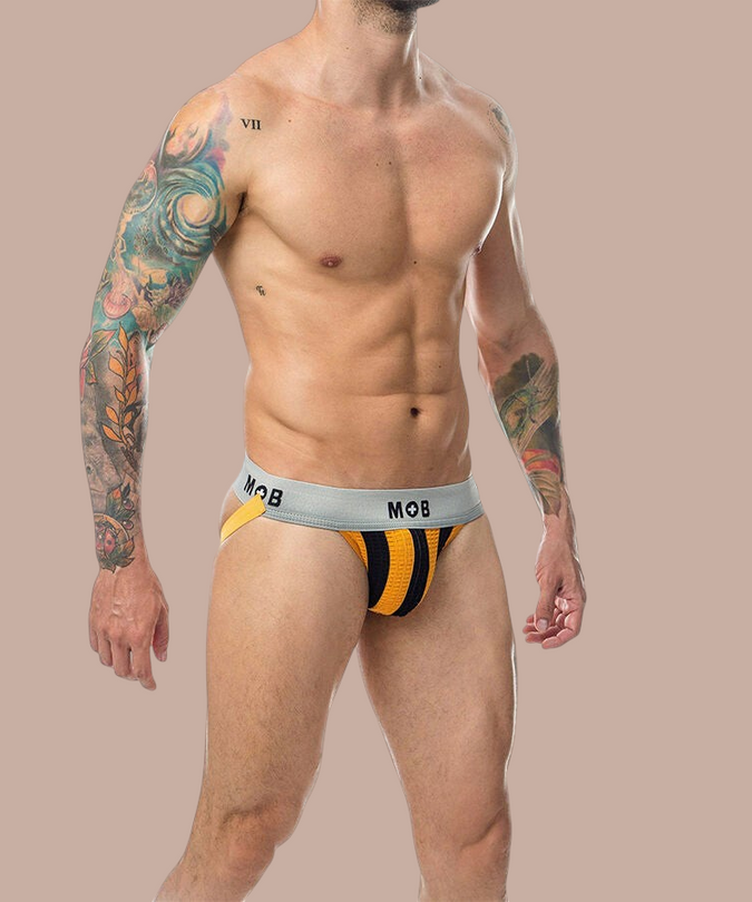 Pleasurements Mob Classic Jock Stripe in oranje met grijze tailleband gedragen door een getatoeëerd model