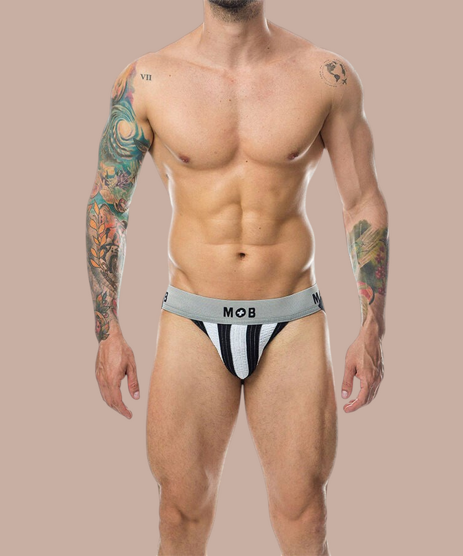 Pleasurements Mob Classic Stripe witte jockstrap met grijze tailleband gedragen door een man met tatoeages