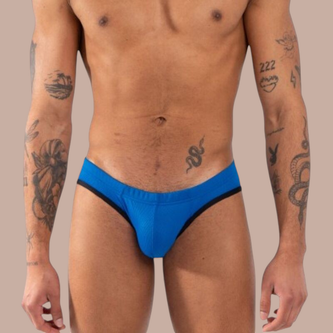 Man draagt een blauwe Pleasurements Burn 018 slip met zwarte accenten voor een verfijnde en sensuele uitstraling.