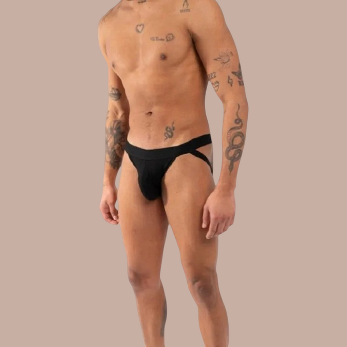 Pleasurements Burn 011 zwarte jockstrap gedragen door een man met tatoeages voor een elegante en sensuele uitstraling.