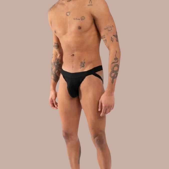 Pleasurements Burn 011 zwarte jockstrap gedragen door een man met tatoeages voor een elegante en sensuele uitstraling.